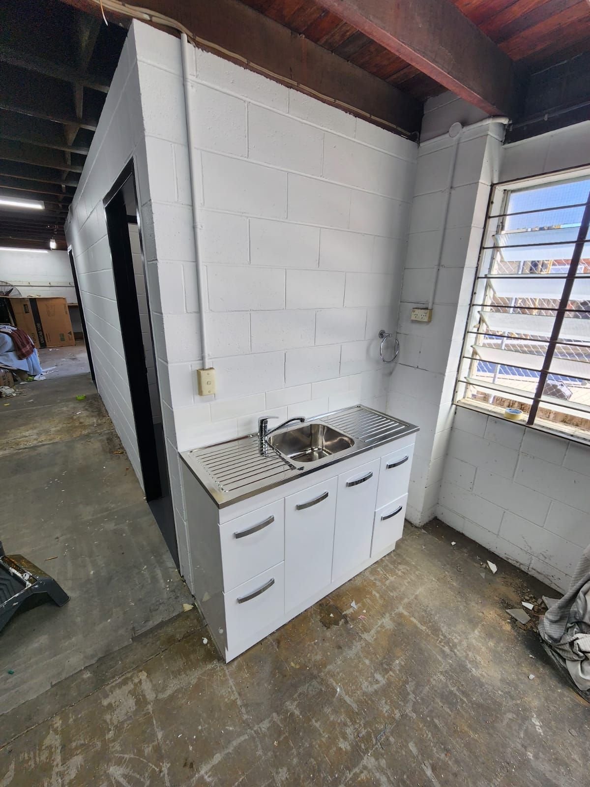 New kitchenette with stainless sink installed against repainted block walls